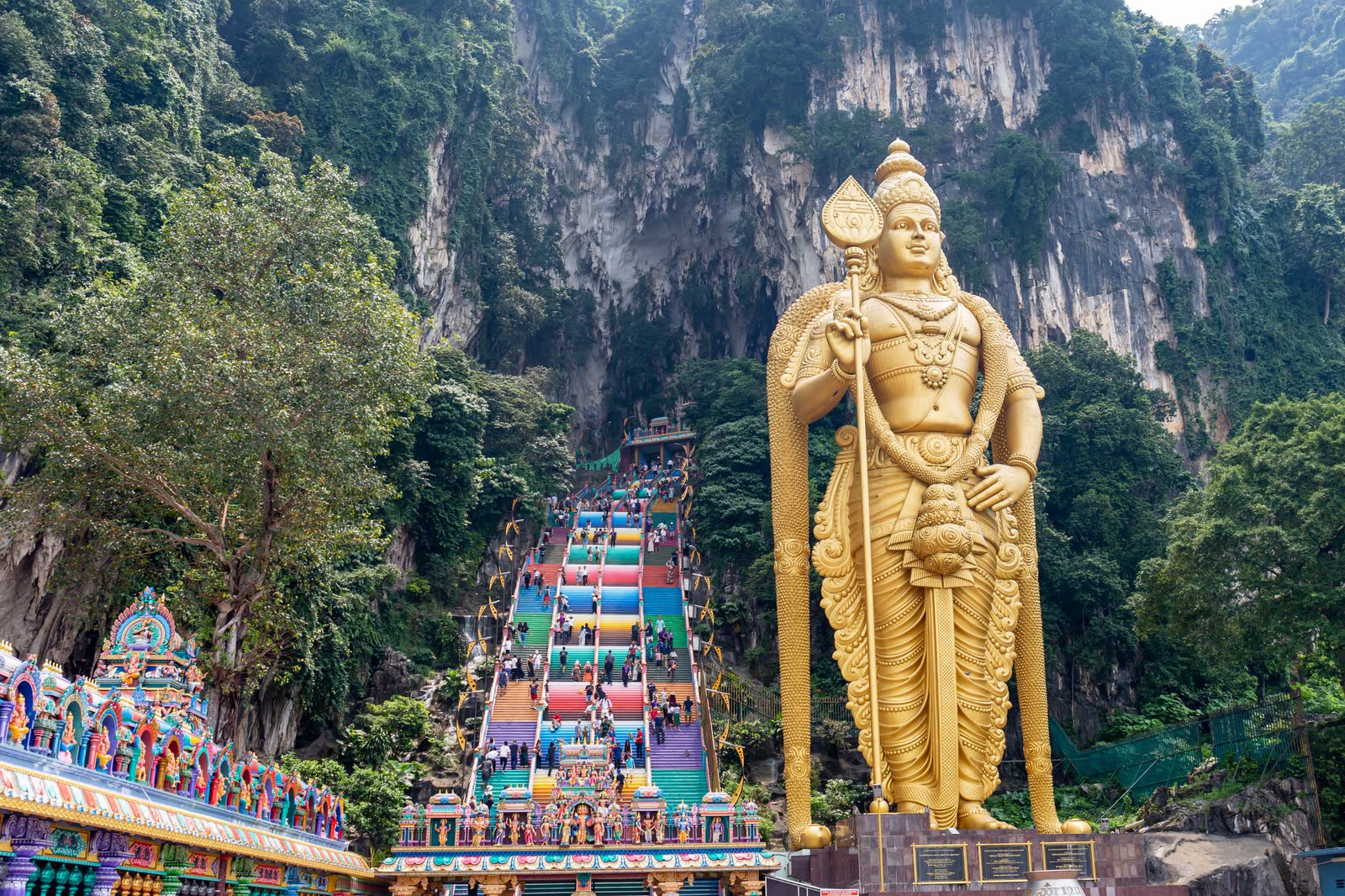 The rainbow-painted staircase climbing into the cliff at Batu Caves, beside the giant golden statue of Lord Murugan.
