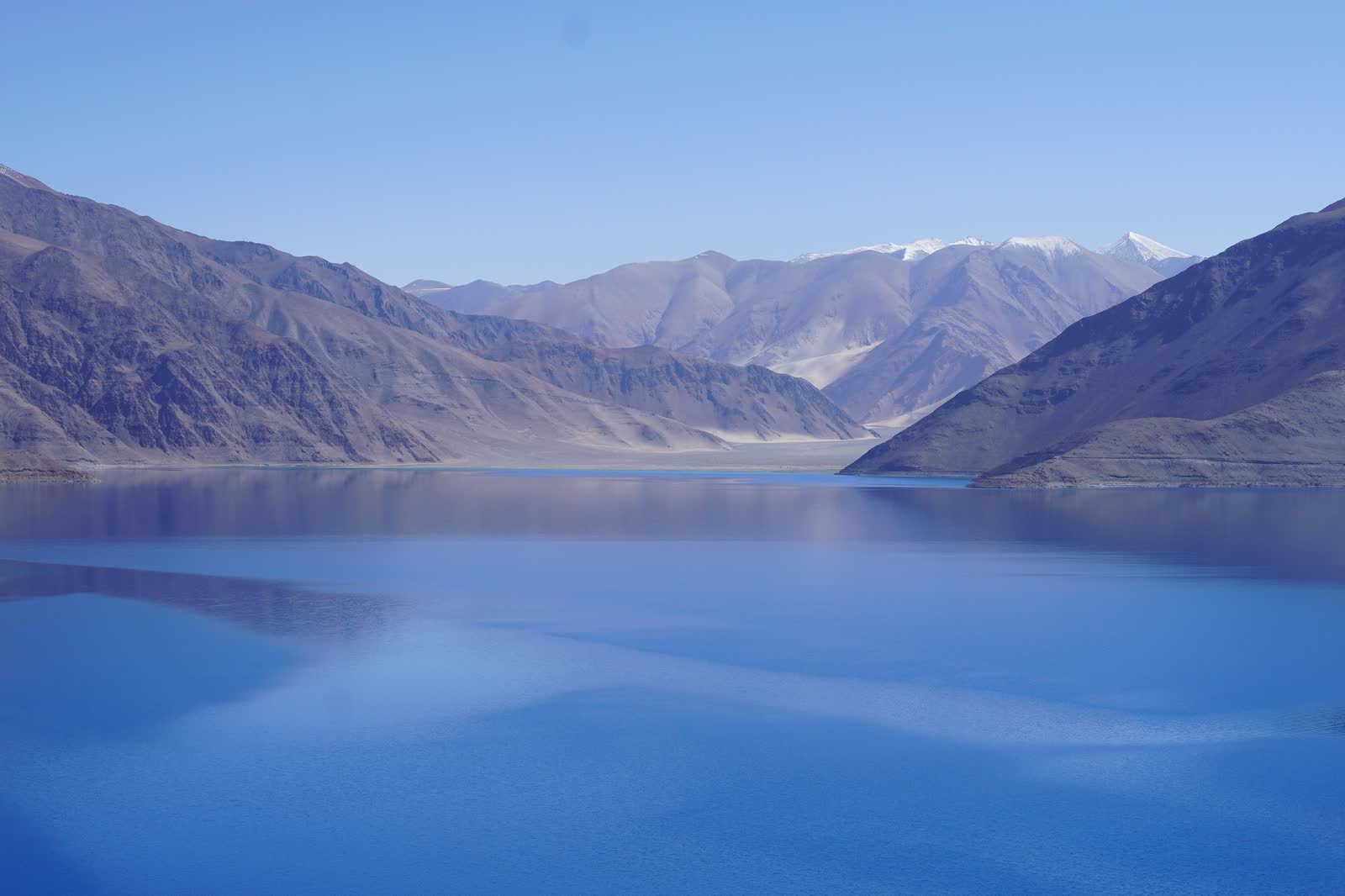 The deep blue water of Pangong Lake, between bare brown mountains, with snow on the peaks beyond.