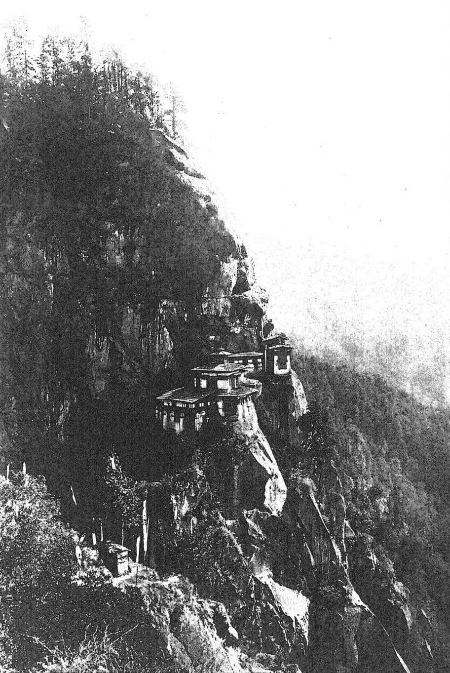 A black-and-white photograph from 1909: Taktsang, the Tiger’s Nest monastery, clinging to a sheer forested cliff.
