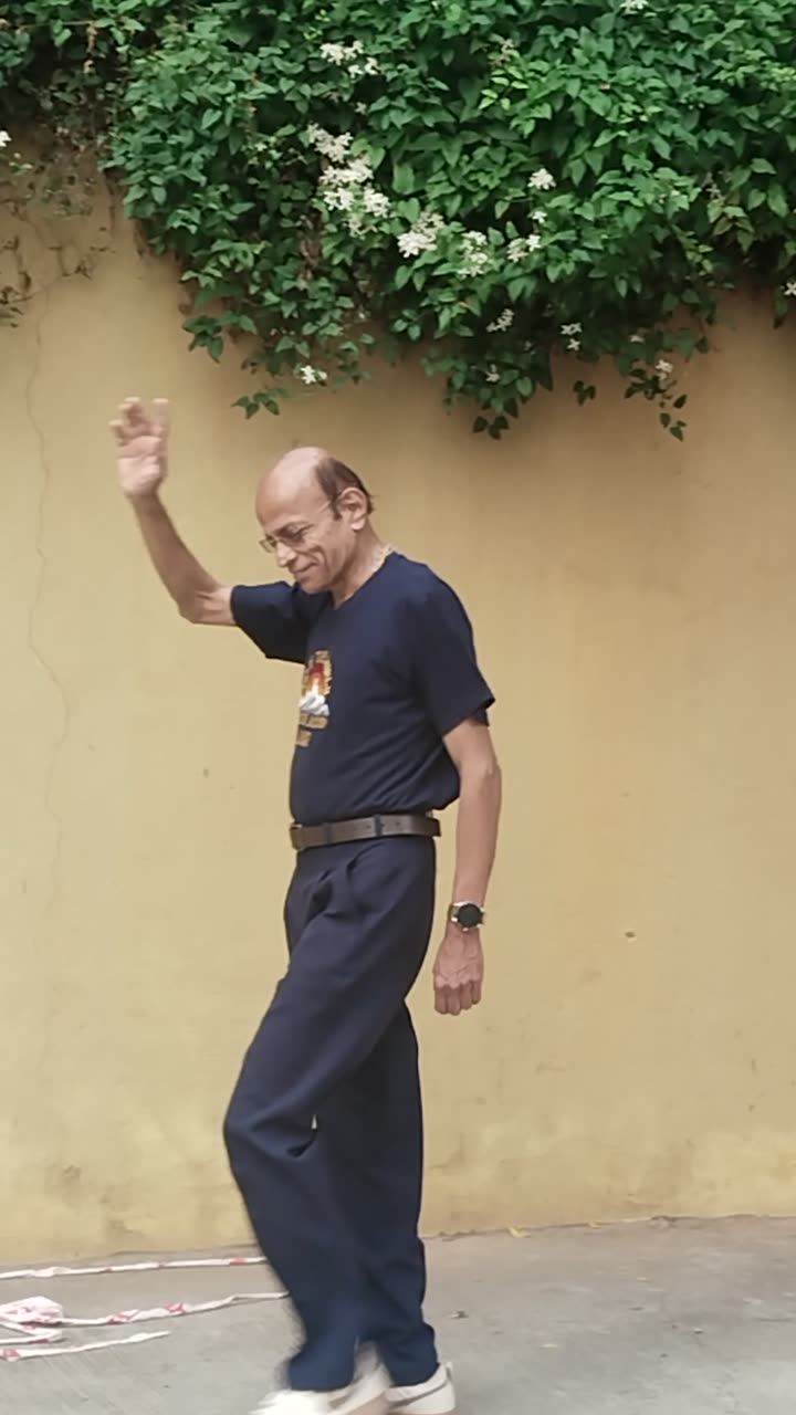 Mid-stride beside the jasmine-topped wall, raising a hand to the camera.